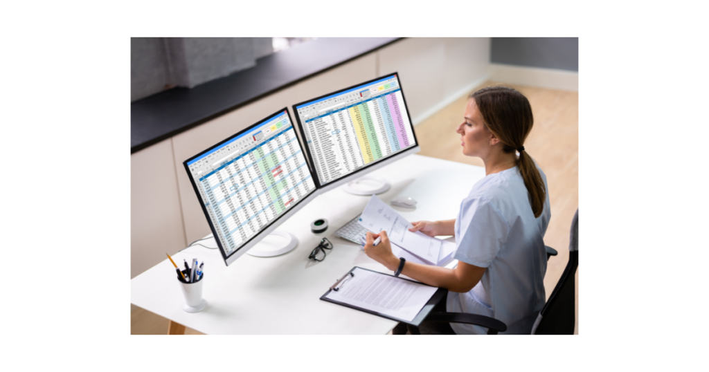 Healthcare professional reviewing electronic health data and documentation on computer screens.