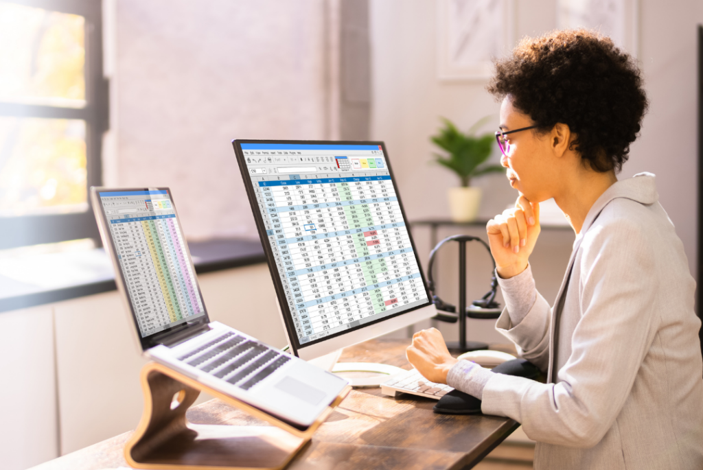 Professional working from home while reviewing data on two computer screens.
