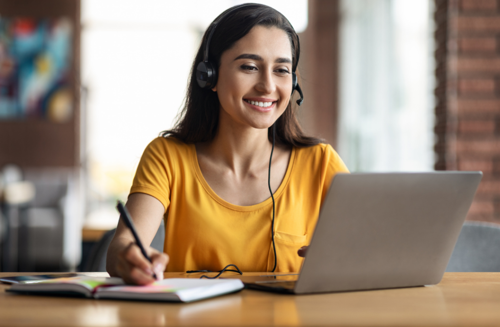 Adult learner using a laptop and taking notes while studying from home.