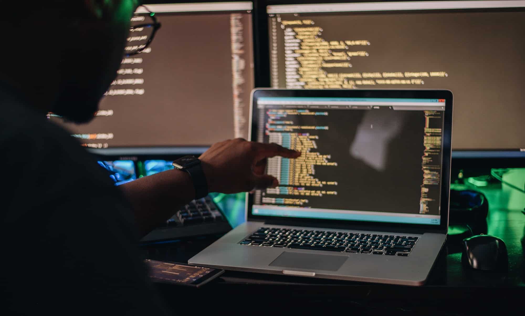 African American man sitting at computer desk looking at computer code, programming, developer